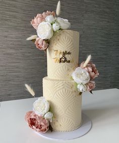 three tiered wedding cake decorated with flowers and feathers on a white tablecloth stand