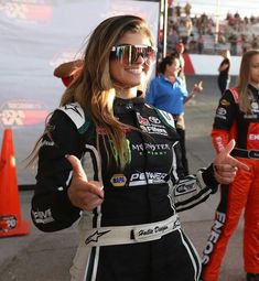 a woman in a racing uniform giving the thumbs up while standing next to other women