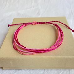 two pink string bracelets sitting on top of a brown box with a white background