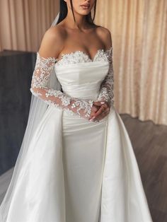 a woman wearing a wedding dress with long sleeves and a veil on her head is posing for the camera