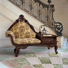 an ornately decorated chair sitting in front of a stair case next to a table with a clock on it