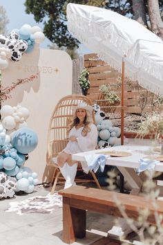 a woman sitting on a chair in front of a table with blue and white balloons