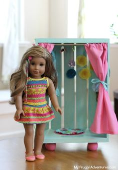 a doll is standing in front of a box with clothes hanging on the door handle