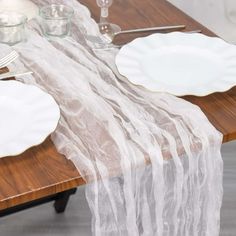 the table is set with white plates and silverware, along with clear glass vases