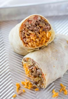 two burritos sitting on top of a metal pan covered in cheese and meat