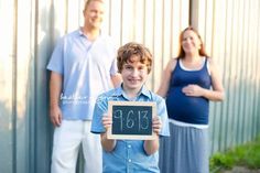 a young boy holding up a chalkboard with the number thirteen on it while two adults stand behind him