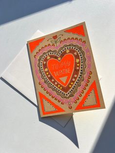 an orange and pink heart shaped valentine's card on top of a white envelope