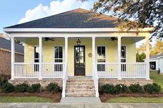 a small yellow house with white pillars and columns on the front porch, along with steps leading up to the front door