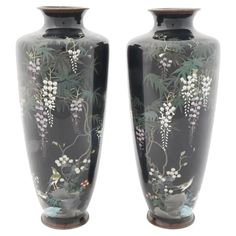 two black vases with white flowers and leaves painted on the sides are facing each other