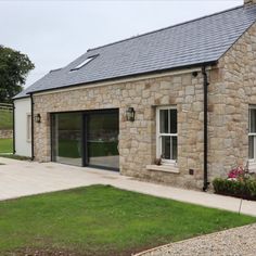 a stone building with two windows and a door on the outside is surrounded by green grass