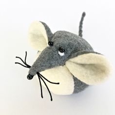 a gray and white felt mouse with black eyes on it's head, sitting in front of a white background