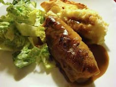 a white plate topped with meat covered in gravy next to a side of salad