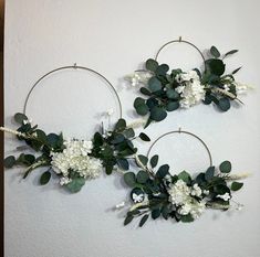 two hoop wreaths with white flowers and greenery hanging on the wall next to each other