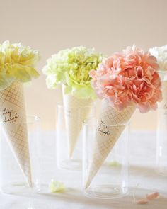 four ice cream cones with flowers in them sitting on a white tableclothed surface