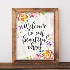 a framed sign that says welcome to our beautiful chaos on it, with flowers in the background