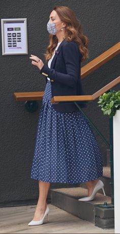 a woman in a blue polka dot dress and white shoes is standing on the stairs