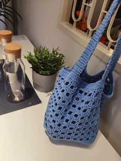 a blue crocheted bag sitting on top of a table next to a potted plant