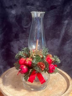 a clear vase with red roses and greenery on a wooden stand in front of a black background