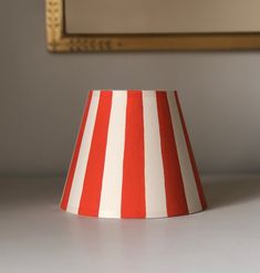 a red and white striped lamp shade sitting on top of a table next to a mirror