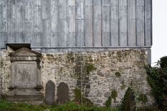 an old stone building with a wooden door in the center and grass growing around it