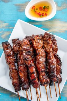 several skewers of meat on a white plate with dipping sauce in the background