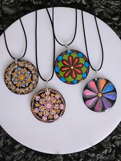 three necklaces on a white plate with black cord hanging from the neck and two are decorated with multicolored flowers