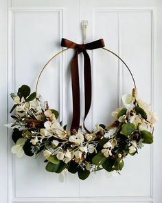 a wreath hanging on the front door with flowers and greenery in it's center