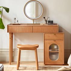 a wooden desk with a mirror and stool next to it on the floor in front of a plant