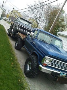 two large trucks parked next to each other on the side of a road in front of a house