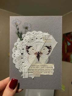 a woman holding up a card with a butterfly on it and some flowers in the background