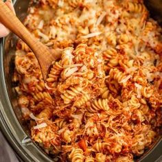 the pasta is being cooked in the crock pot with a wooden spoon to stir it