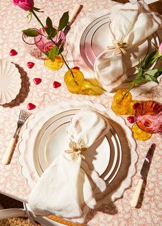 the table is set with white plates and pink napkins, silverware and flowers