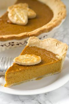 a slice of pumpkin pie on a white plate with a fork next to the pie