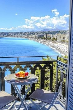 two chairs and a table with fruit on it overlooking the ocean from an apartment balcony