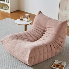 a pink chair sitting on top of a rug next to a table with a magazine