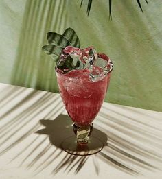 a red glass filled with liquid sitting on top of a table next to a palm tree