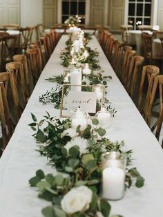 a long table with candles and greenery on it is set up for a formal dinner