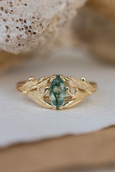 a gold ring with a green stone in the center on top of a white rock