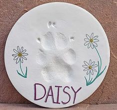 a white plate with the word daisy painted on it and a paw print in purple