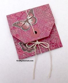 a pink envelope with a butterfly on it and string attached to the front, sitting on a white surface