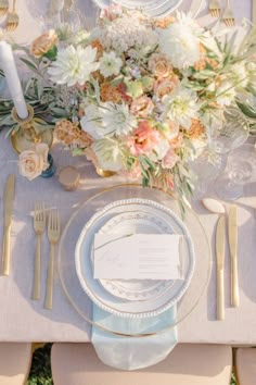 the table is set with silverware, plates and floral centerpieces on it