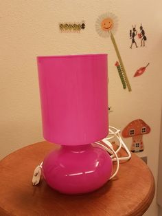 a bright pink vase sitting on top of a wooden table next to a white wall