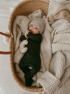 a baby is laying in a basket on the bed and wearing a knitted hat