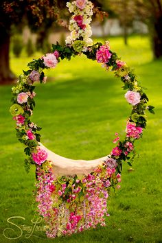 a wreath with pink flowers and greenery hanging from it's sides in the grass