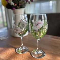 two wine glasses sitting on top of a wooden table next to a vase with flowers