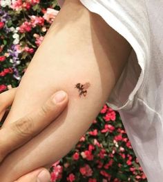 a person holding their arm with a small tattoo on it's left side, in front of some flowers