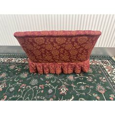 a red couch with ruffles on it sitting on top of a green rug