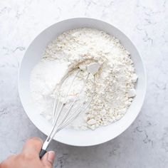 a bowl filled with flour and whisk being stirred by a hand on the side