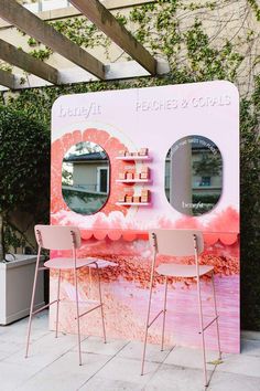 two chairs are sitting in front of a pink counter with mirrors on it and plants behind them