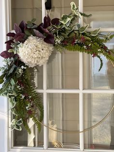 a wreath with flowers and greenery hanging on a window sill in front of a house